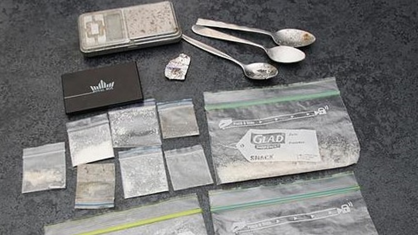 packets of drugs and spoons are on an evidence table