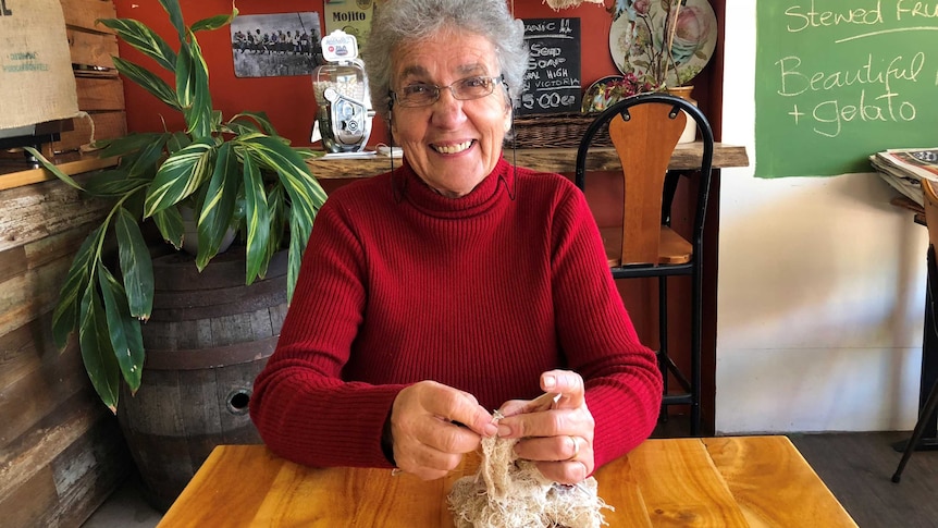 lady sitting at a table in a cafe knitting a scarf made from tea bag strings
