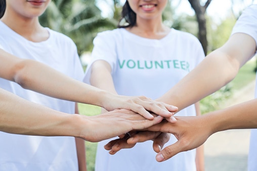 Five hands stack on top of each other in a gesture of working together 