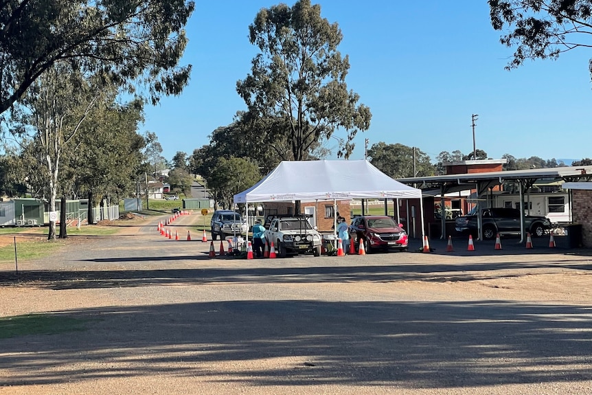 Cars line up for covid testing under a shade cover stands people in PPE.