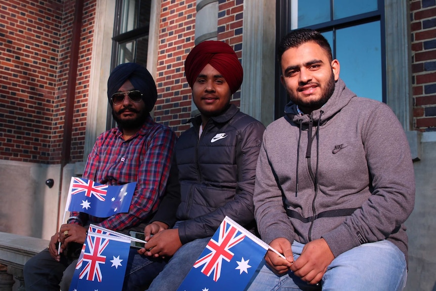 Three men, two wearing Sikh turbans, sit waiting for the Anzac Day parade through Perth.