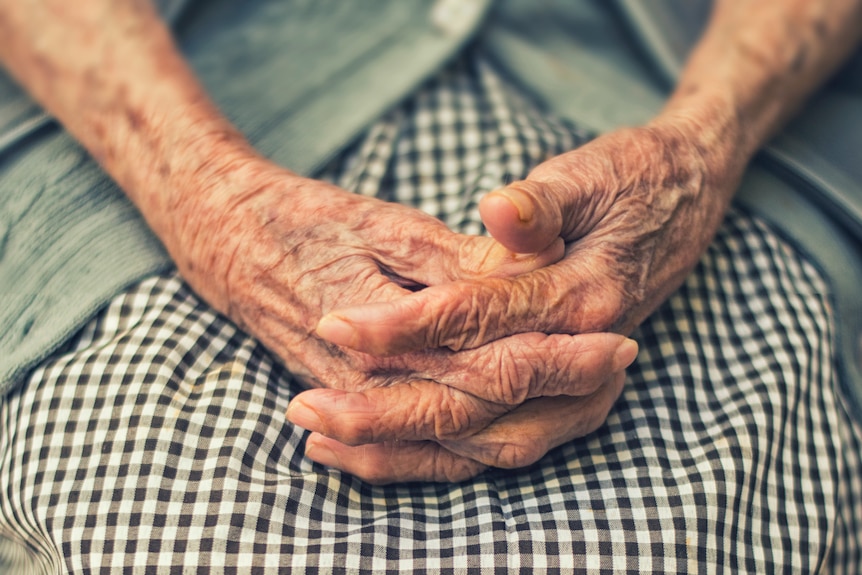 A stock shot of an older woman clasping her hands together