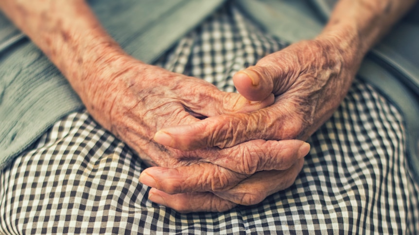 A stock shot of an older woman clasping her hands together