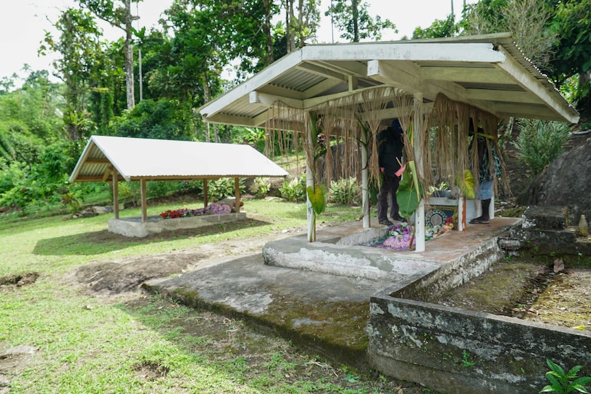 A man and a woman stand on either side of a grave.