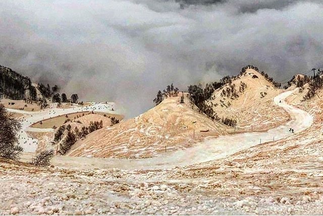 Ski slopes covered with orange snow and surrounded by clouds.