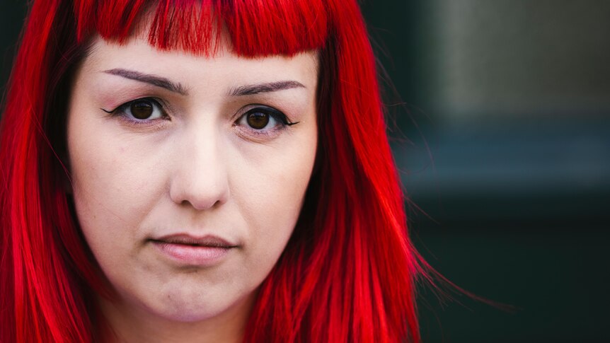 A close-up of a woman with red hair, staring straight into the camera.