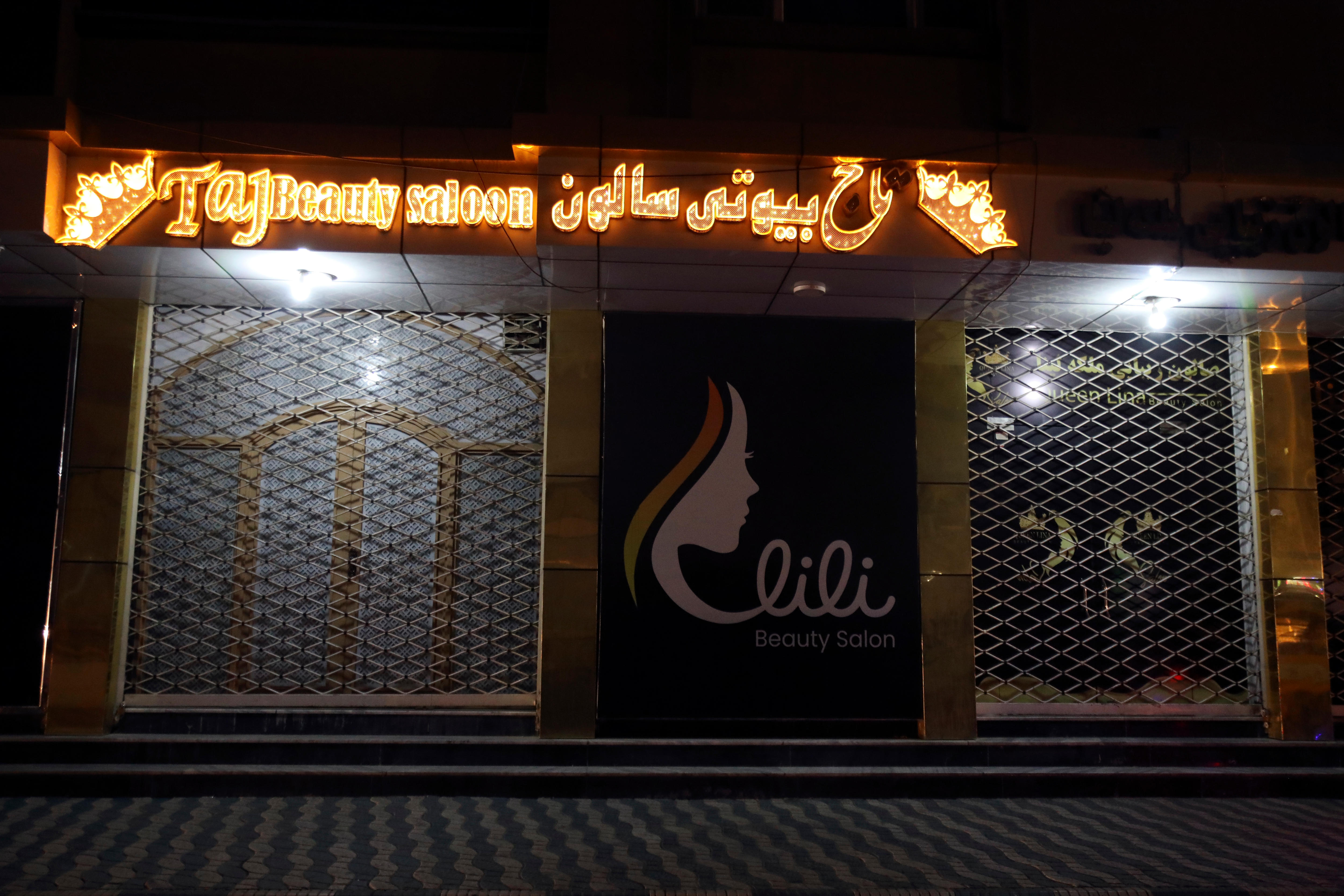 a closed shop in the night with an orange neon sign at the top saying Taj beauty salon