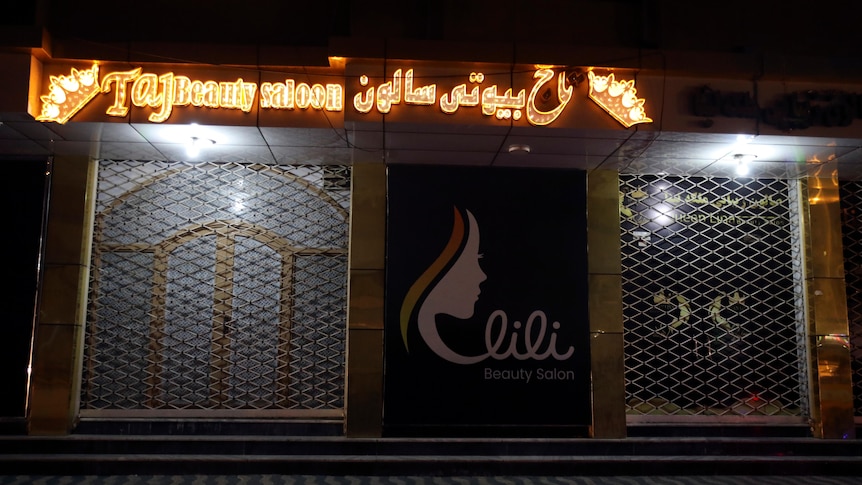 a closed shop in the night with an orange neon sign at the top saying Taj beauty salon