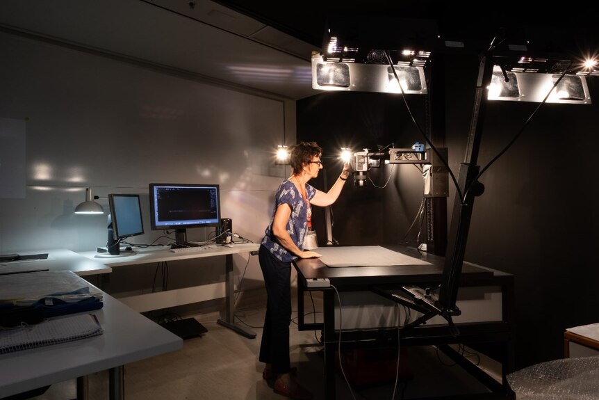 A woman sets up a digitisation station with camera and lights in a dark room