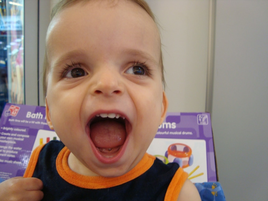 A young boy opening his mouth wide and smiling. Looks like he is laughing. 