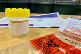 A yellow sterile container used for a saliva test surrounded by a plastic bag and pieces of paper.