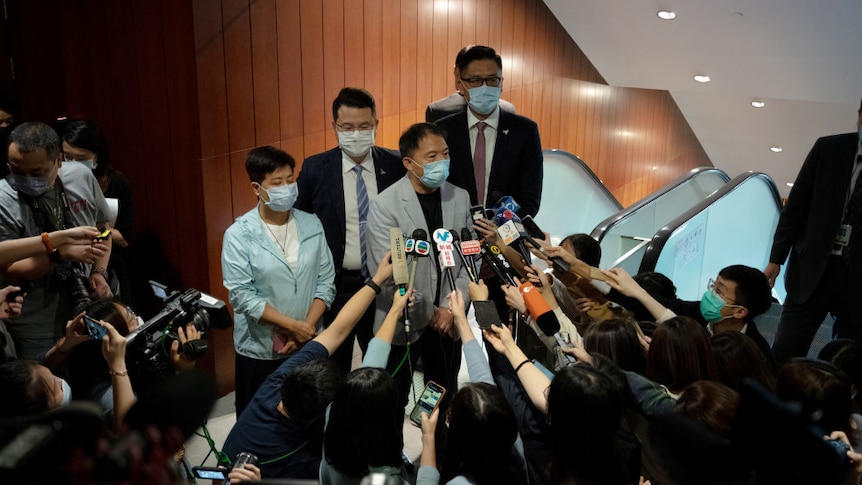 Four pro-democracy lawmakers wearing masks address a mass of journalists with their microphones stretched out to them