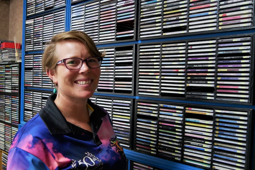 A woman stands smiling in front of stacks of CDs