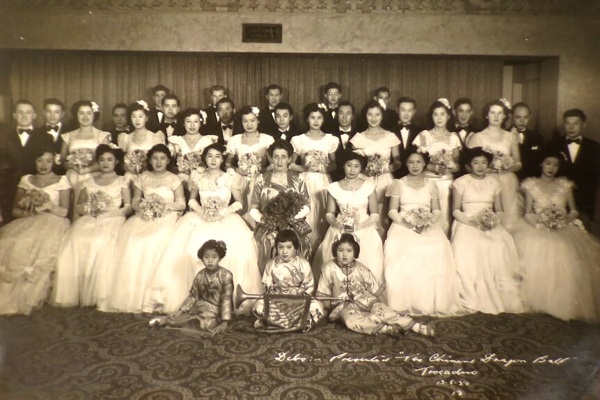 Four rows of debutantes in white dresses and their partners pose for pictures