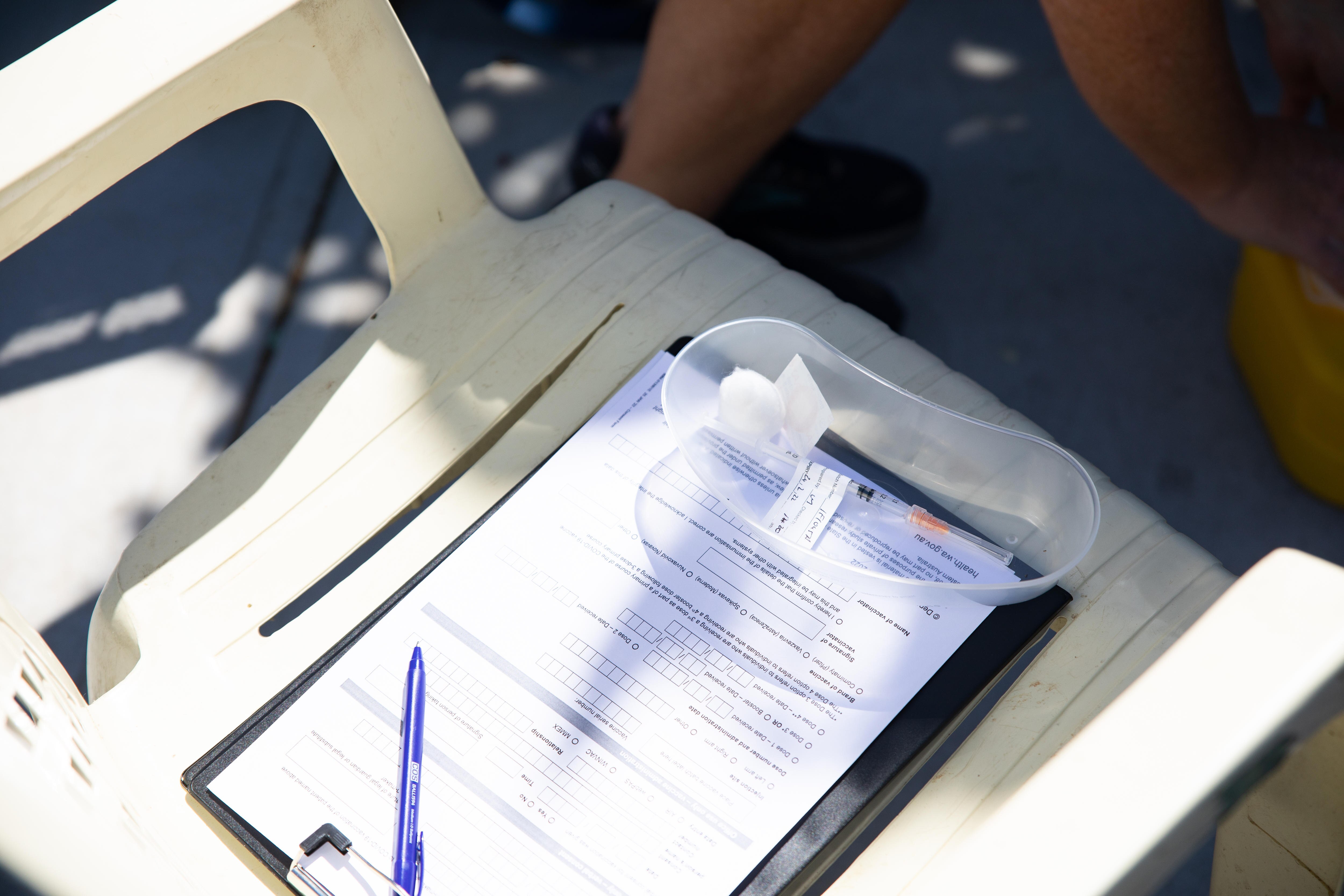 A vaccine sits in a plastic tray on top of a clipboard on a plastic chair.