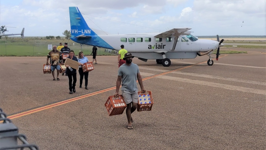 People carrying supplies walk off an small plane in Fitzroy Crossing.