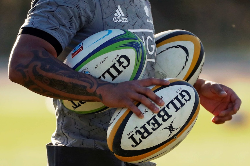 The tattooed arm of a New Zealand's All Blacks player, who is holding three footballs.
