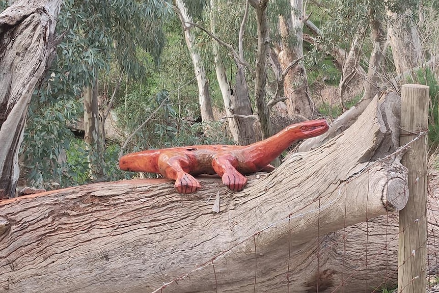 A large wooden lizard sculpture sits on top of a fallen tree