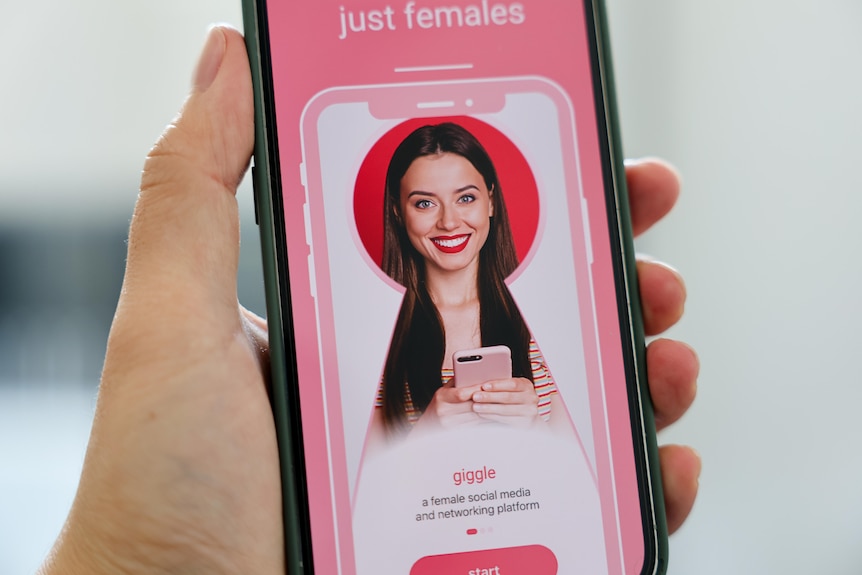 A social media application opened up on a phone depicting a woman smiling at the camera while holding a phone.