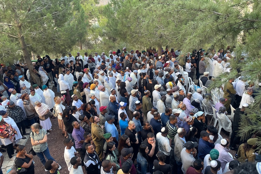 A crowd of people gathered beneath tall trees in a Jerusalem cemetery