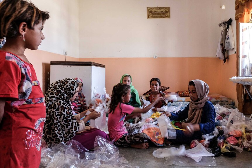 Women sit on the ground sorting underwear for distribution among displaced people.
