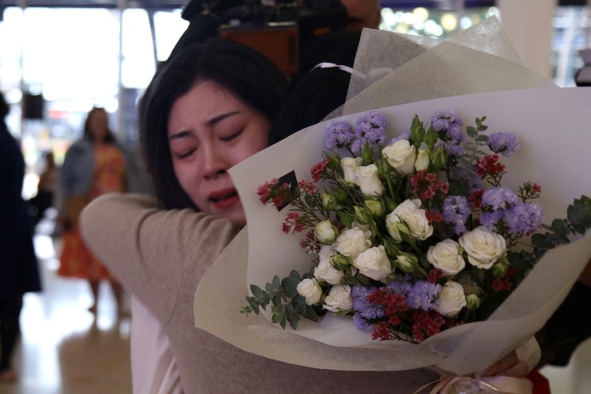 A woman closes her eyes as she holds a bunch of flowers and hugs someone.