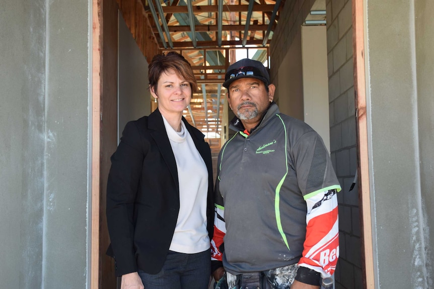 Woman and man stand side by side in the doorway of a half constructed house