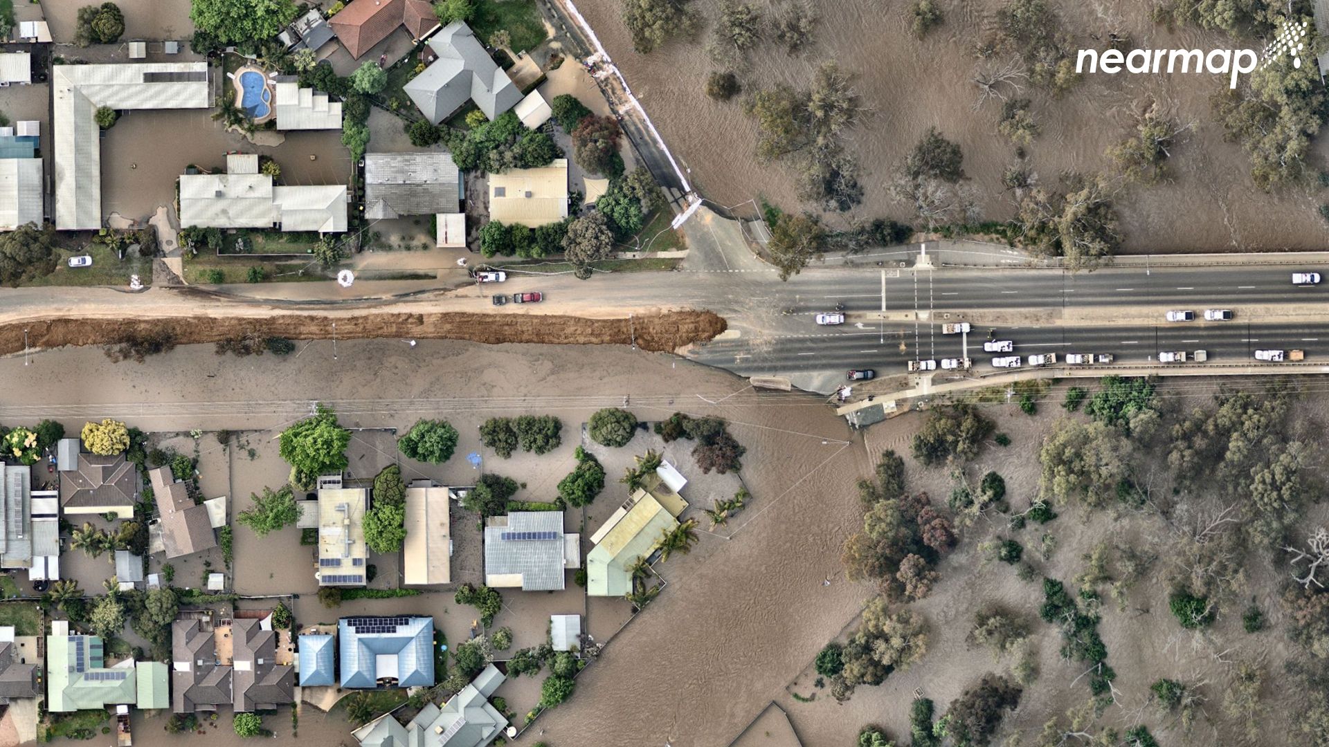 Floodwater can be seen surrounding homes and ripping a road apart after the river burst its banks