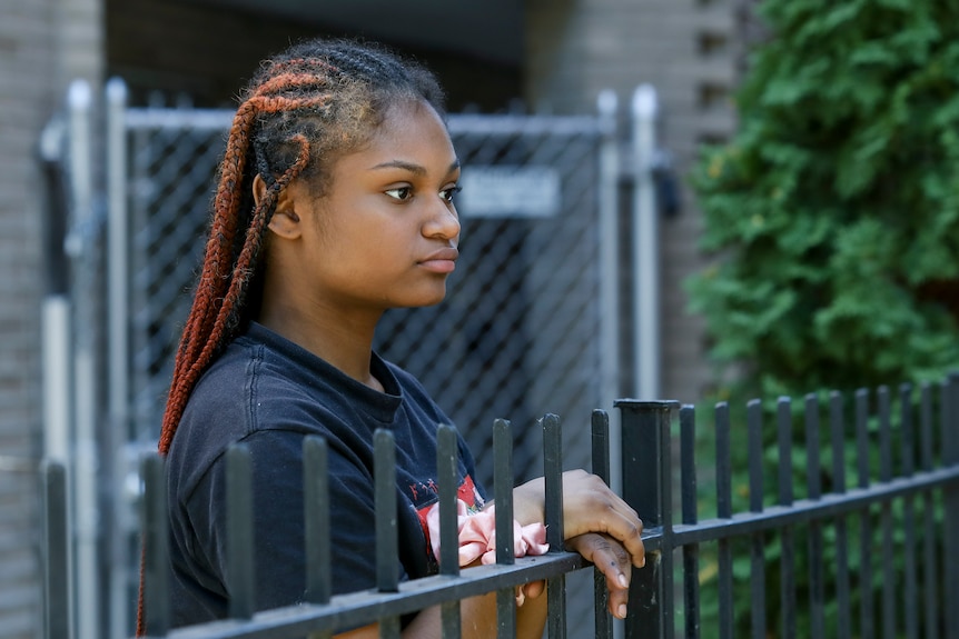 Teenage woman holds a fence wearing a black top.