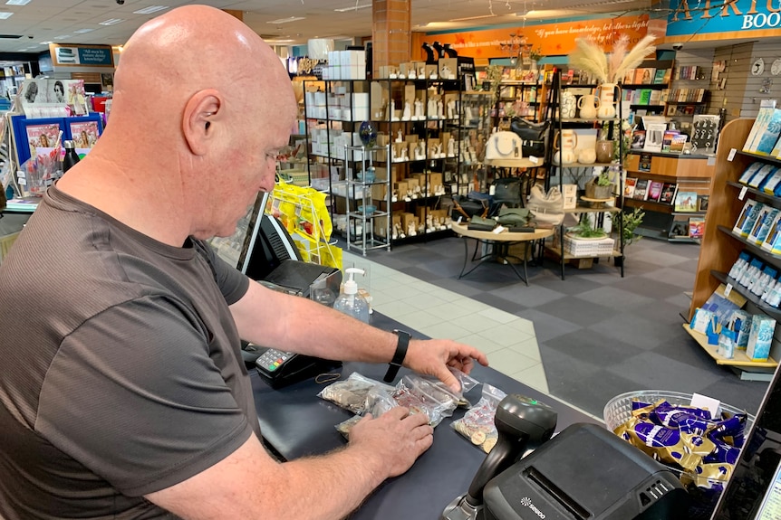 A man counting bags of coins in a newsagency