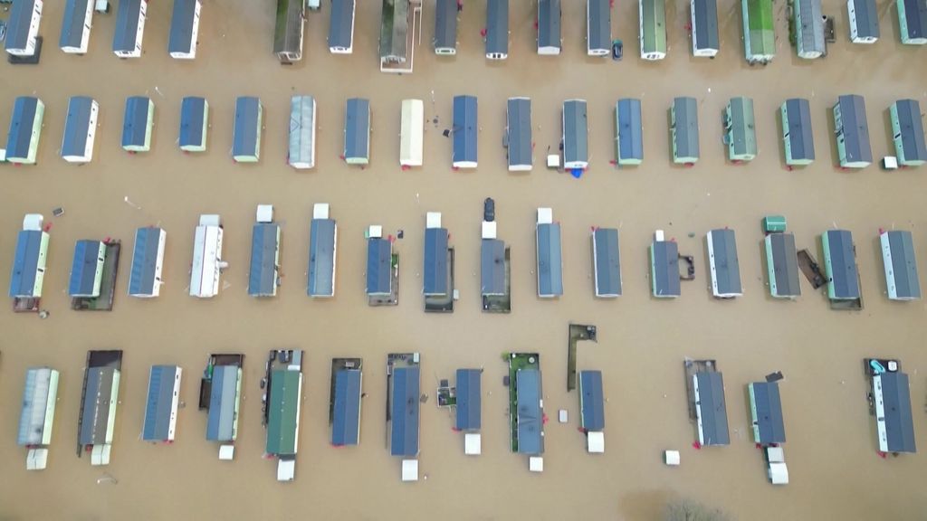 Drone footage shows only rows of houses' roofs with brown floodwater surrounding them.