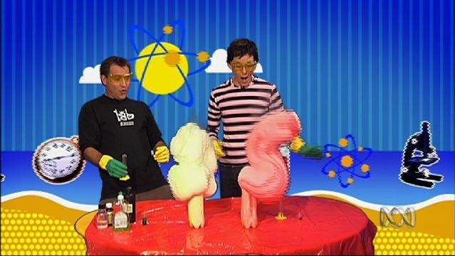 Two men look amazed at foamy substance exploding from top of soft drink bottles