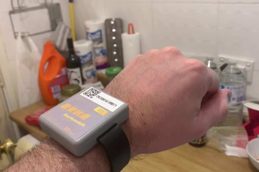 A fore arm with a Hong Kong coronavirus tracking wristband with blurry kitchen items in the background