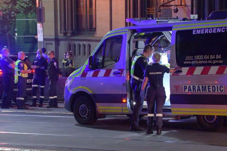 An ambulance surrounded by police officers in Melbourne CBD at night.
