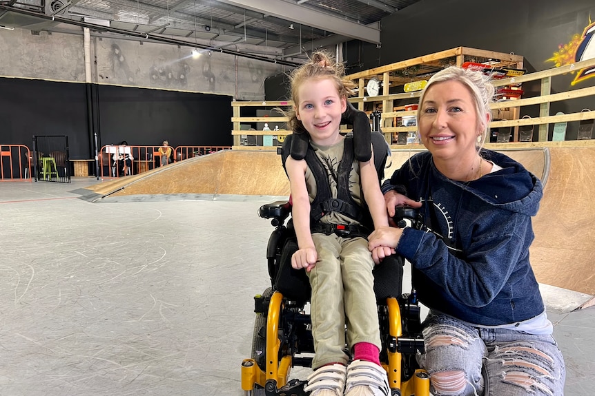 Girl smiling in wheelchair with her mother next to her smiling at camera