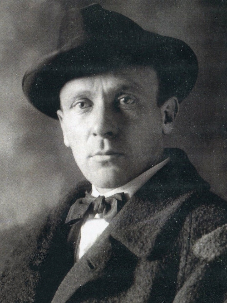 A black and white photo of Mikhail Bulgakov who wears a bow tie and a hat.