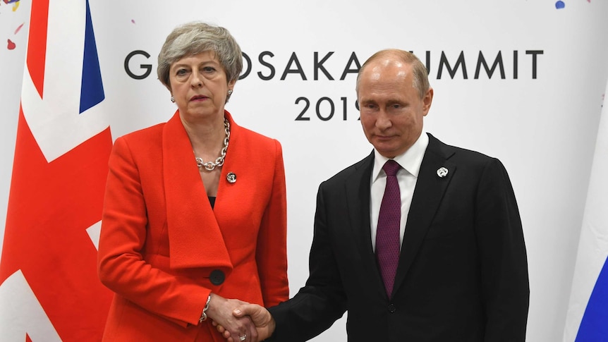 Theresa May wearing a bright red suit unenthusiastically shakes hands with Vladimir Putin.