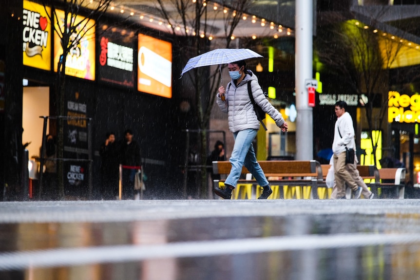 Un homme traverse la route sous la pluie avec un parapluie