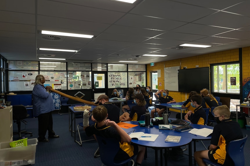 Elder players digeridoo to to Year 8 students attentively listening.