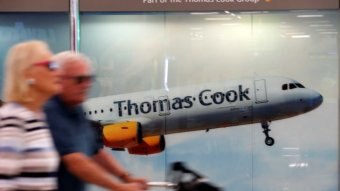 Passengers are seen at Mallorca Airport walking past a Thomas Cook sign.