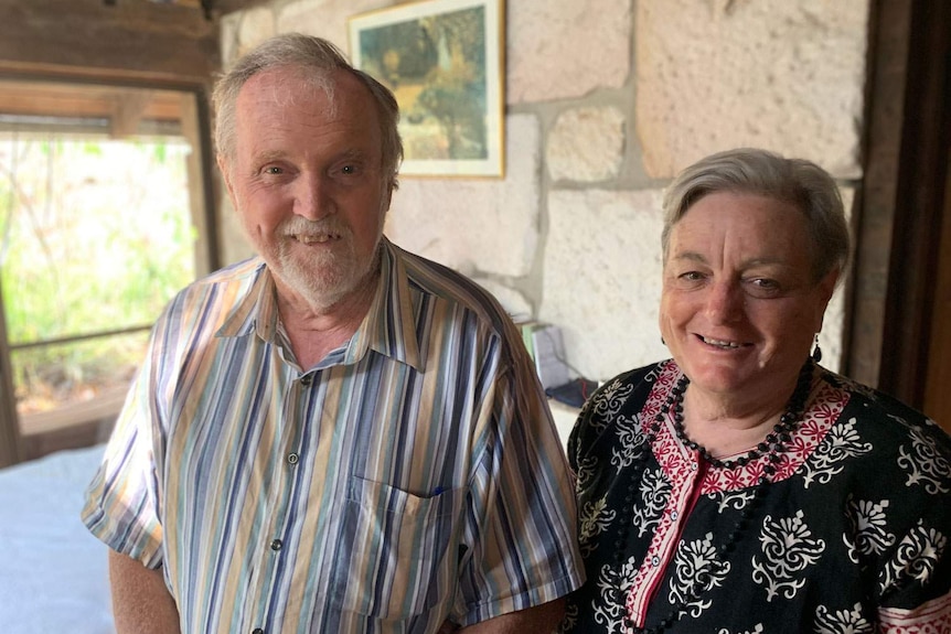 Ken and Harriet Aitken stand smiling in a room at their house.