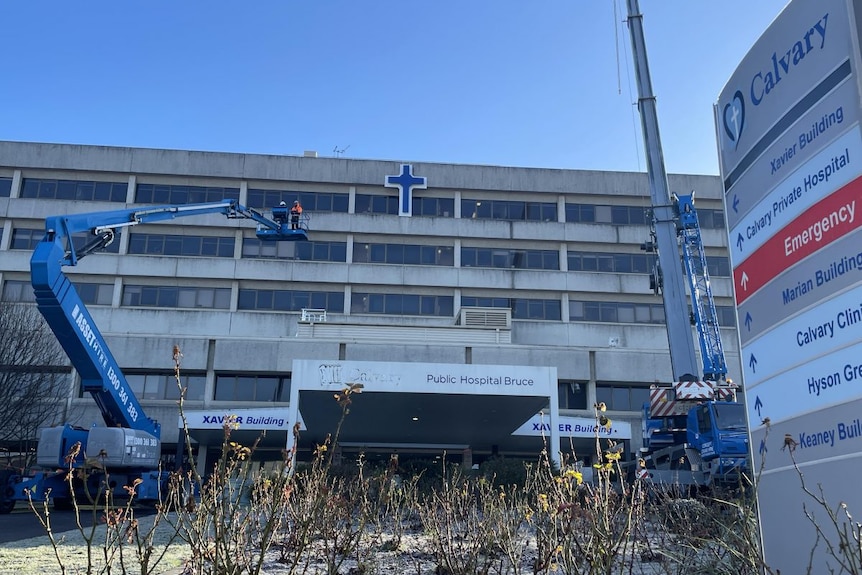 Workers in a blue cherry picker reaching up to a cross on a building. 
