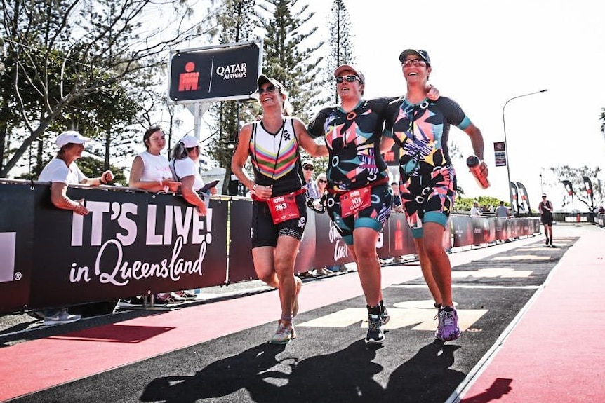 Three women running toward a triathlon finish line