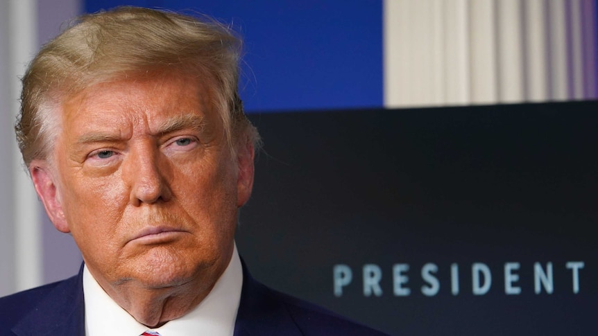 President Donald Trump listens during an event in the briefing as he stands in front of sign that reads 'President'.