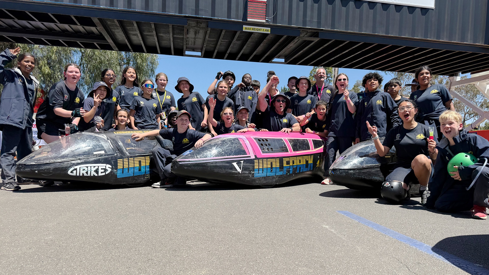 About 30 kids pose for a photo next to three human powered bikes which look like miniature bullet train carriages.