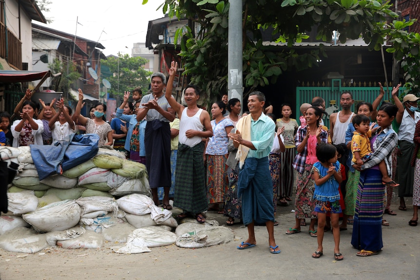 Residents gesture with a three-fingers salute, a symbol of resistance, as protesters march past them.