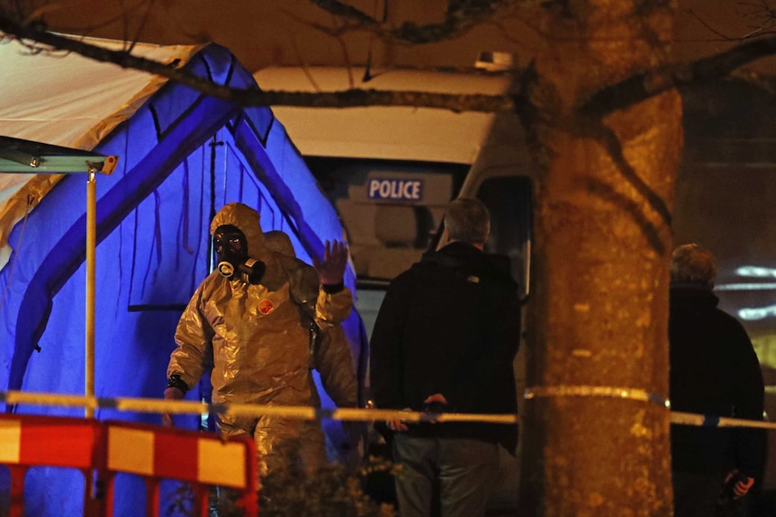 Investigators in chemical hazmat suits walk next to a police tent.