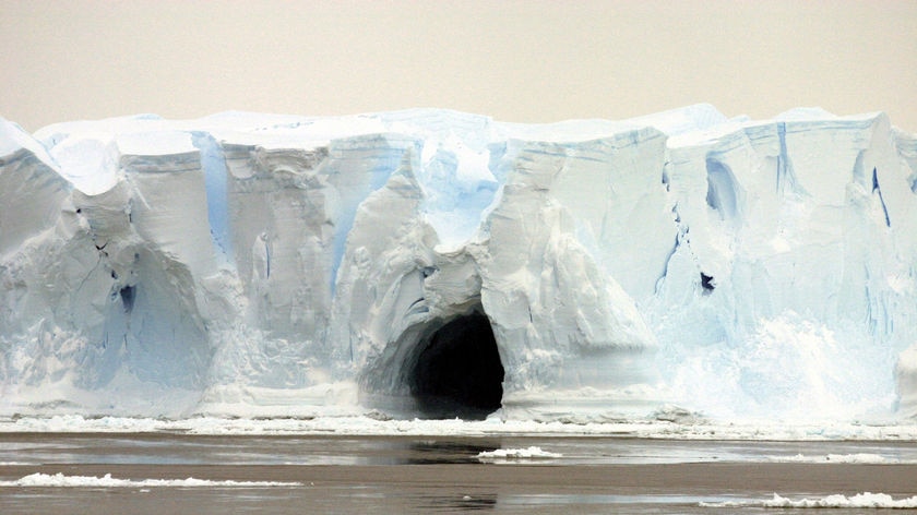 An ice cave yawns from the pit of a sagging iceberg in Antarctica.