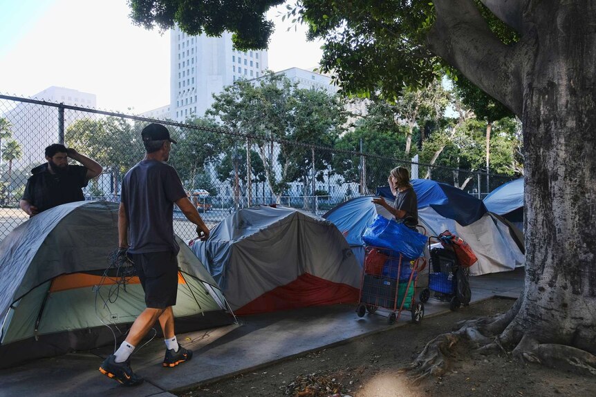 A row of tents line up a street as a woman stands with her belongings stashed in a shopping trolley.