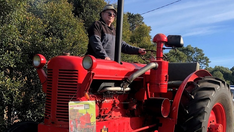 A bright red tractor emits exhaust fumes while a man sits on top.